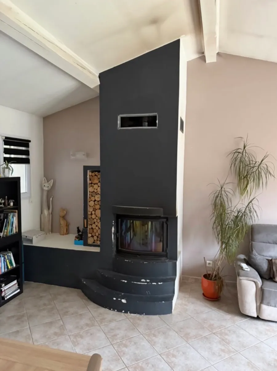 Séjour occupé par une grande cheminée d’angle noire avec insert, avant démolition